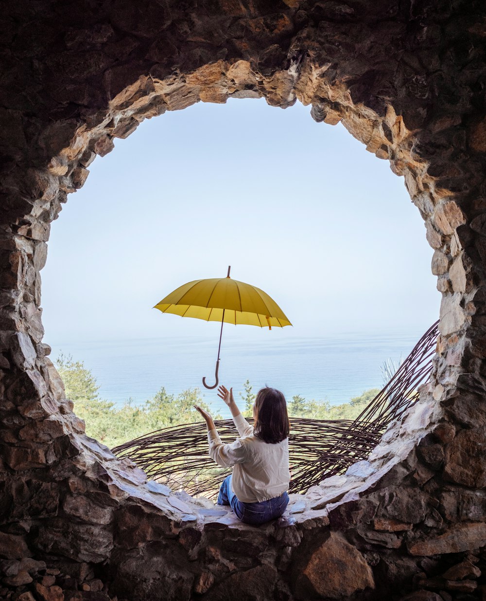 a woman sitting on a rock wall holding an umbrella