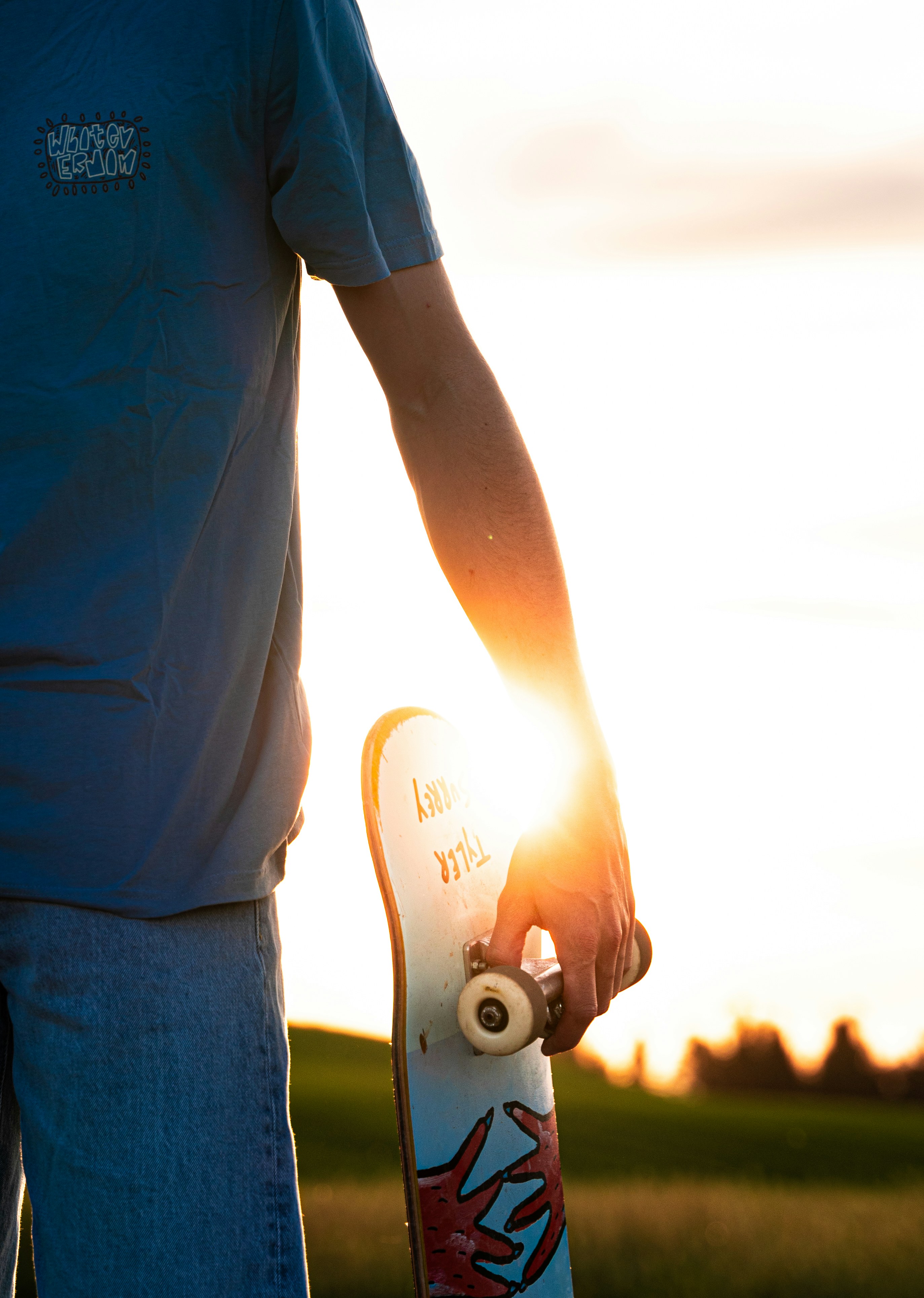 a person holding a skateboard with the sun setting in the background