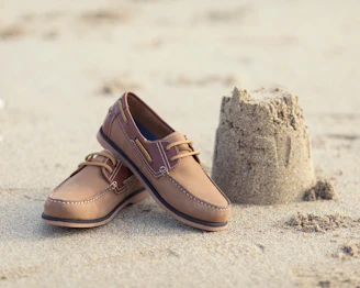 a pair of brown shoes sitting on top of a sandy beach