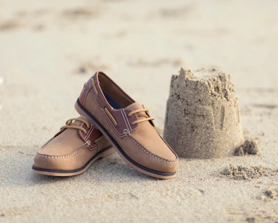 a pair of brown shoes sitting on top of a sandy beach