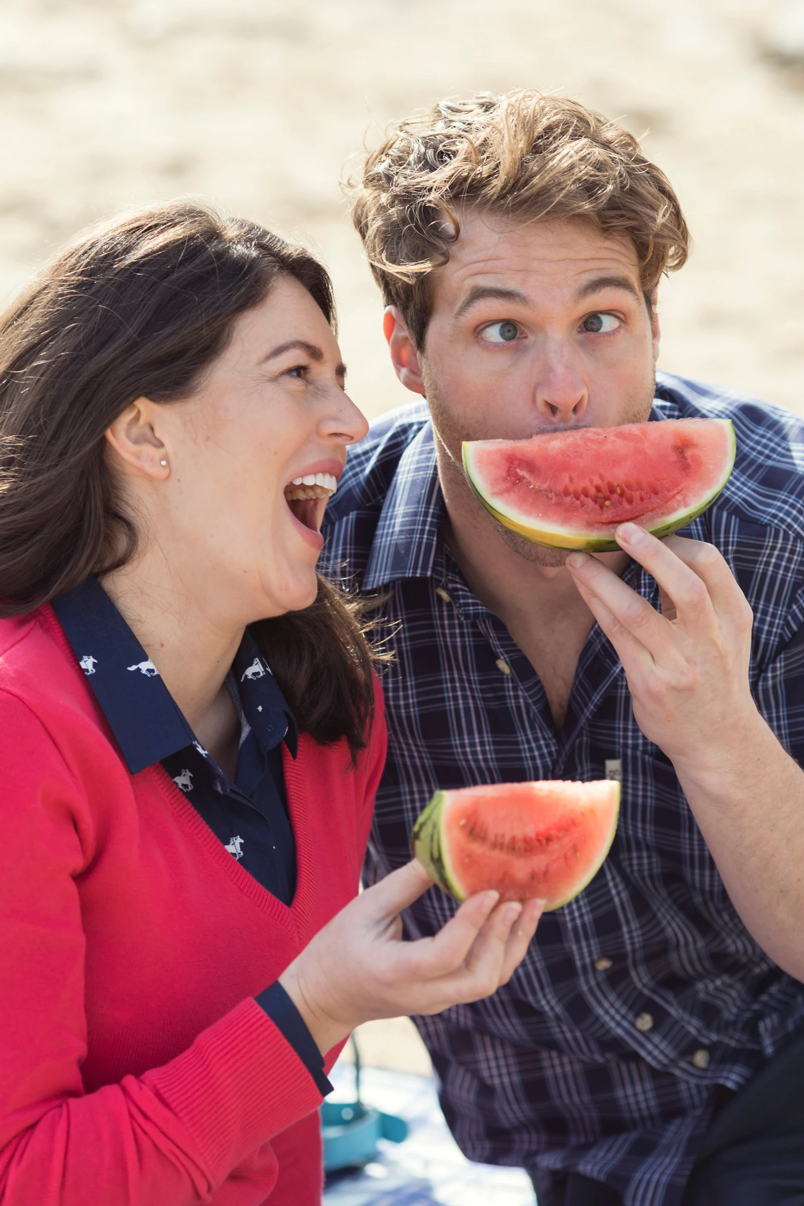 A man and a woman laughing together while eating slices of watermelon
