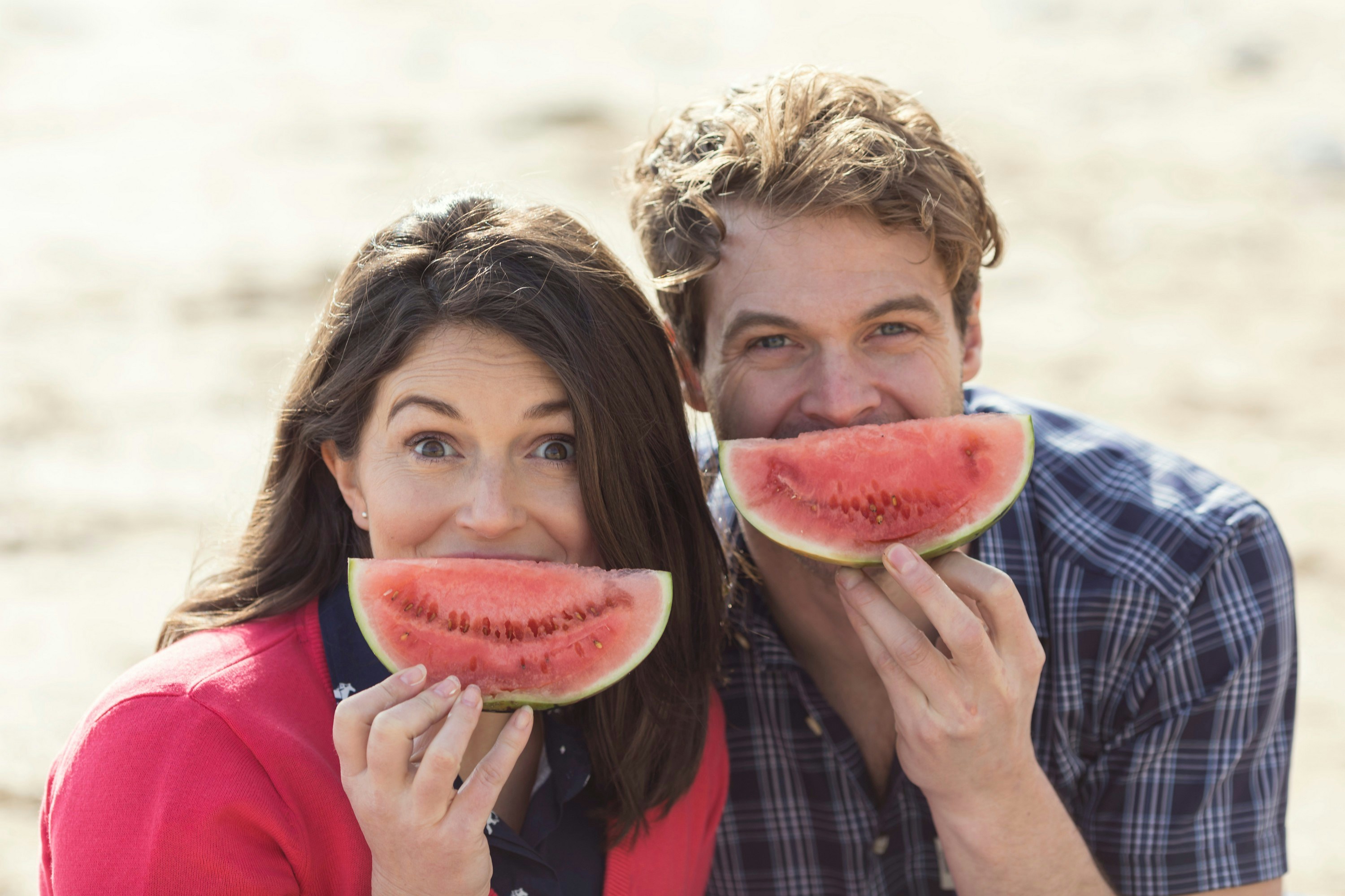a man and a woman eating watermelon on the beach