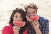 a man and a woman eating watermelon on the beach