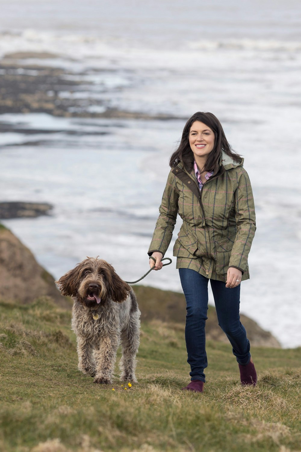 바다 근처에서 목줄을 매고 개를 산책시키는 여성