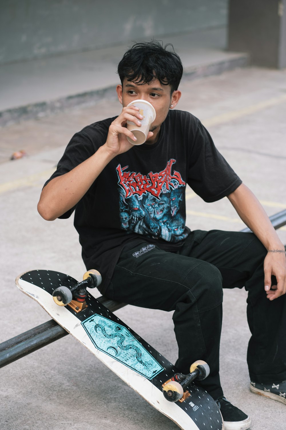 a young man sitting on a skateboard drinking from a cup