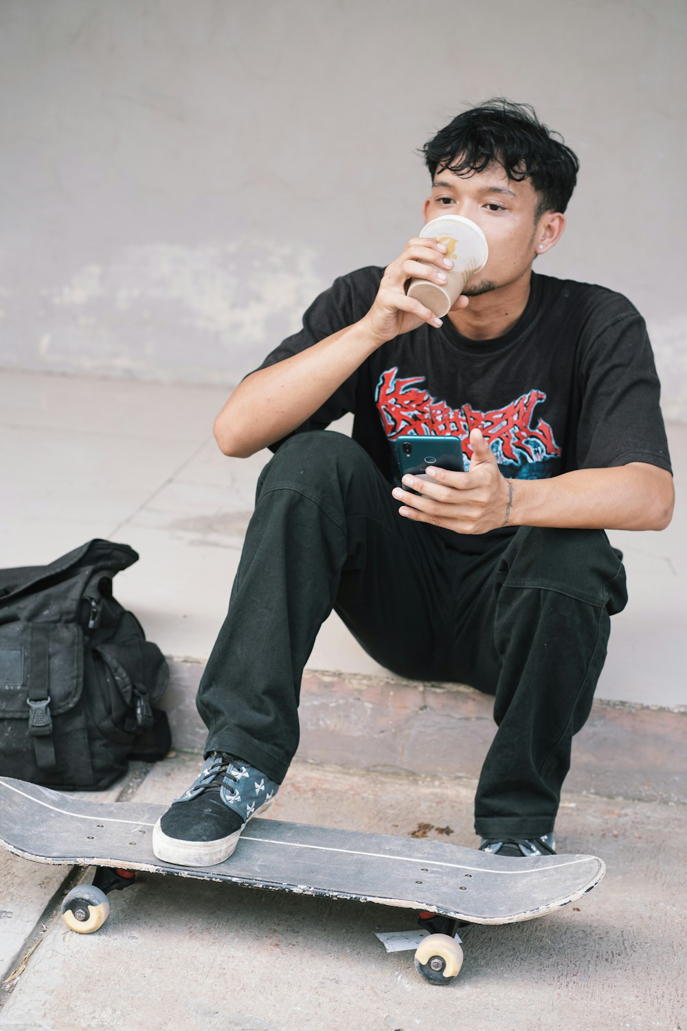 a man sitting on a skateboard drinking from a cup
