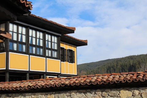 a yellow building with a brown roof and a mountain in the background