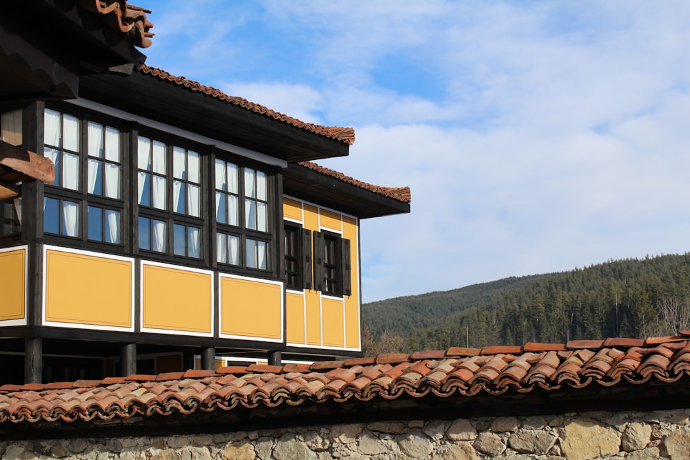 a yellow building with a brown roof and a mountain in the background