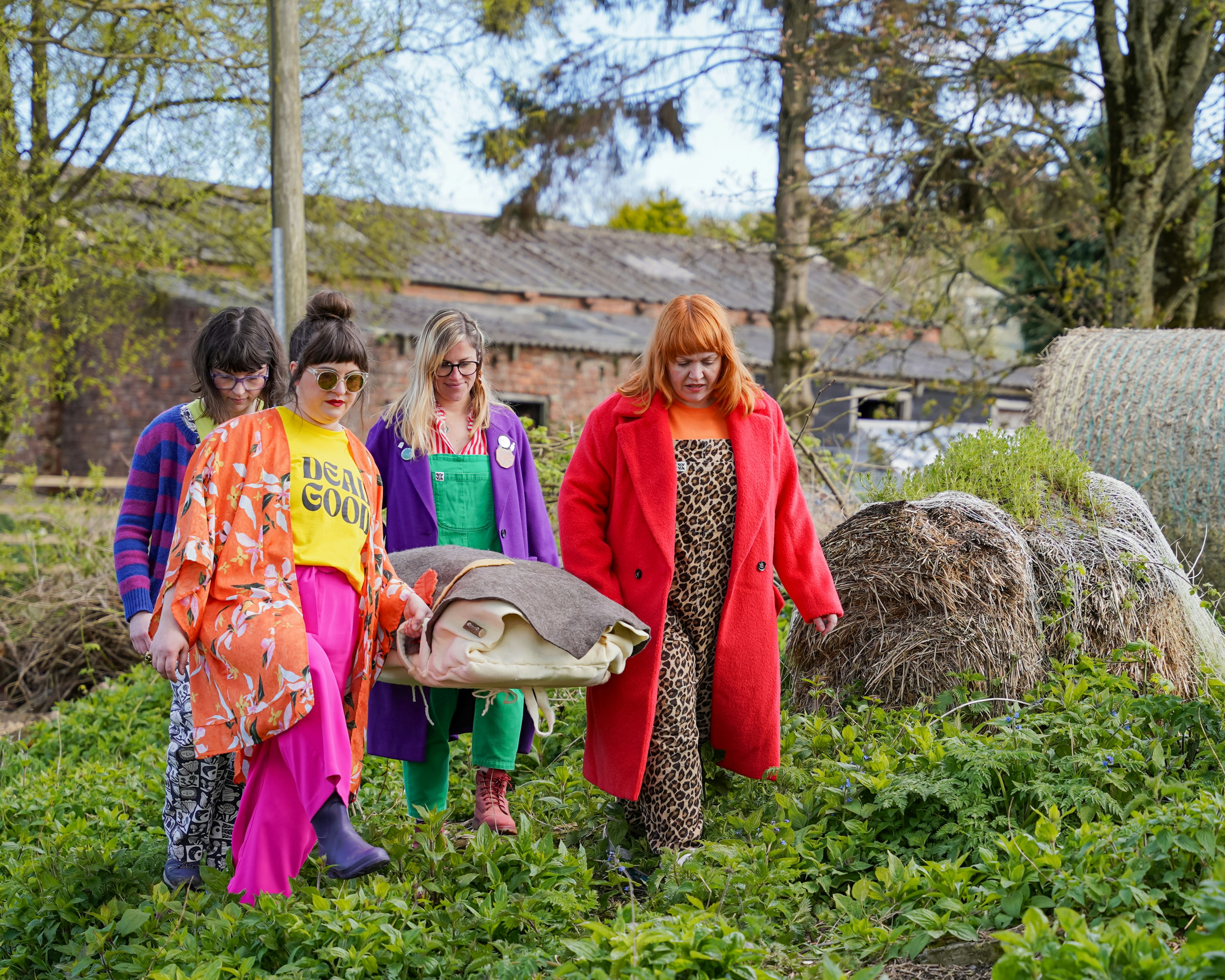 Four friends in bright clothing carrying a woollen felt shroud in a woodland burial setting (County Durham, UK). Sarah Johnson Photography.