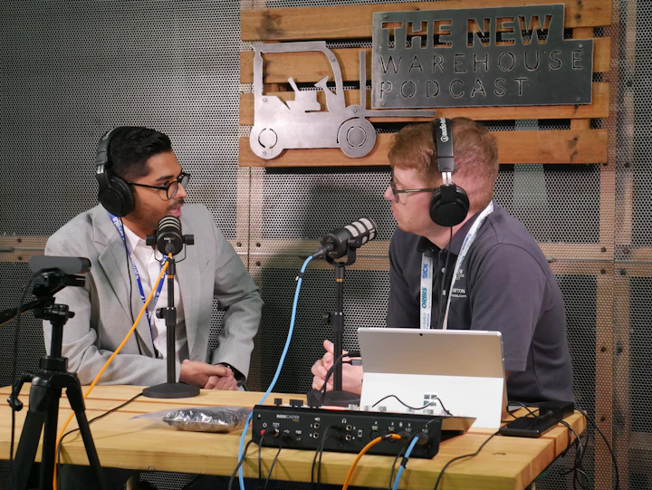 Two hosts seated at microphones across a table, recording a long-form conversation