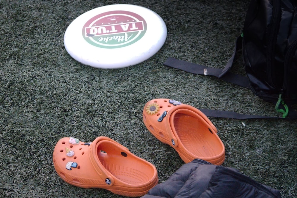 a pair of orange clogs sitting next to a frisbee