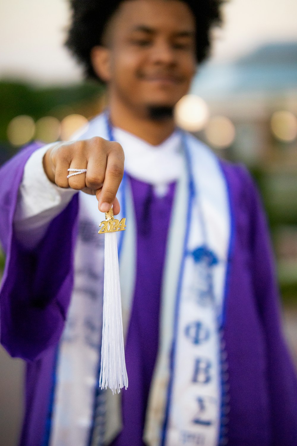 a man in a purple graduation gown points at the camera
