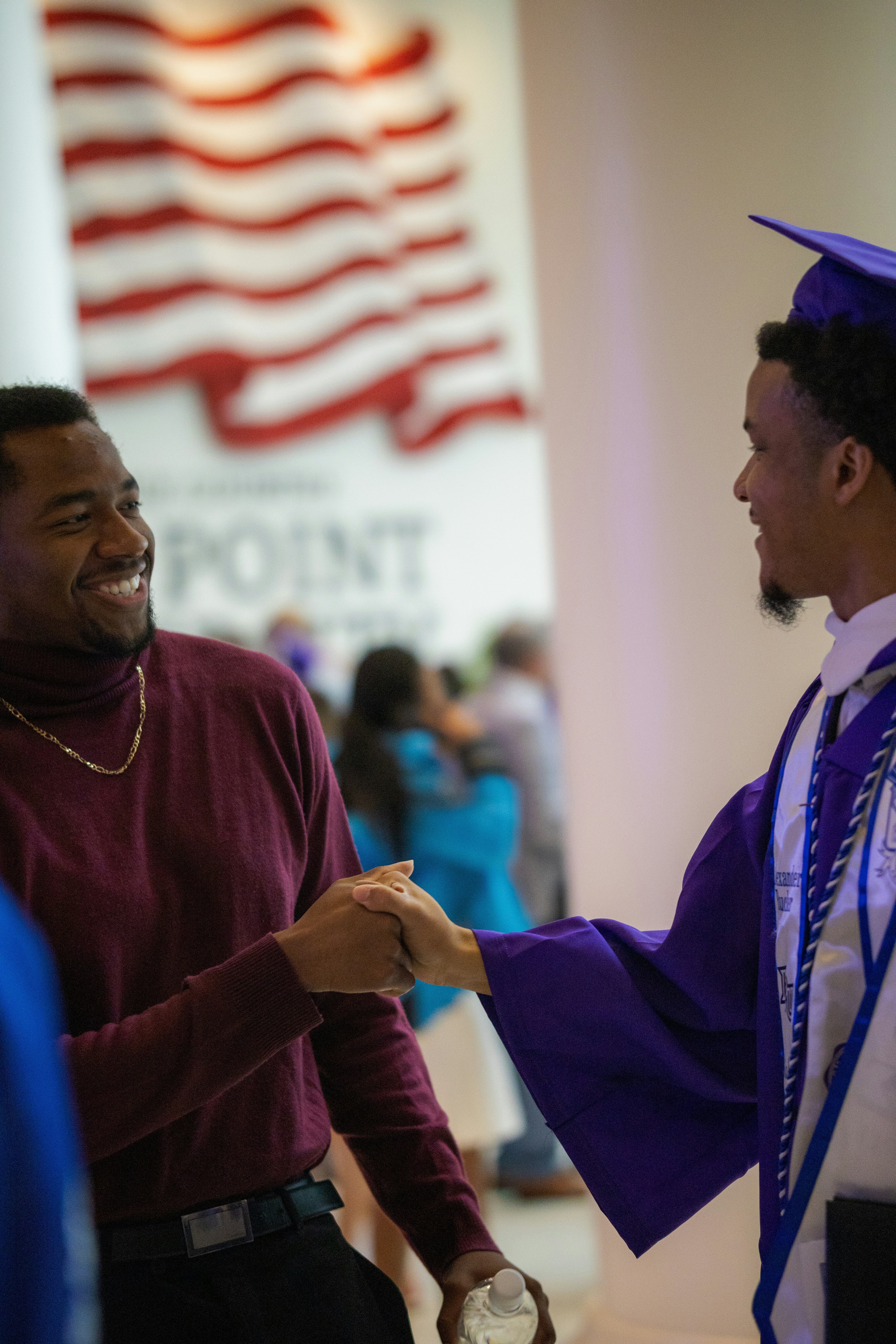 a man in a graduation cap and gown shaking hands with another man