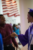 a man in a graduation cap and gown shaking hands with another man