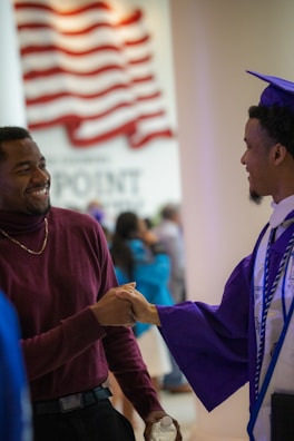 a man in a graduation cap and gown shaking hands with another man