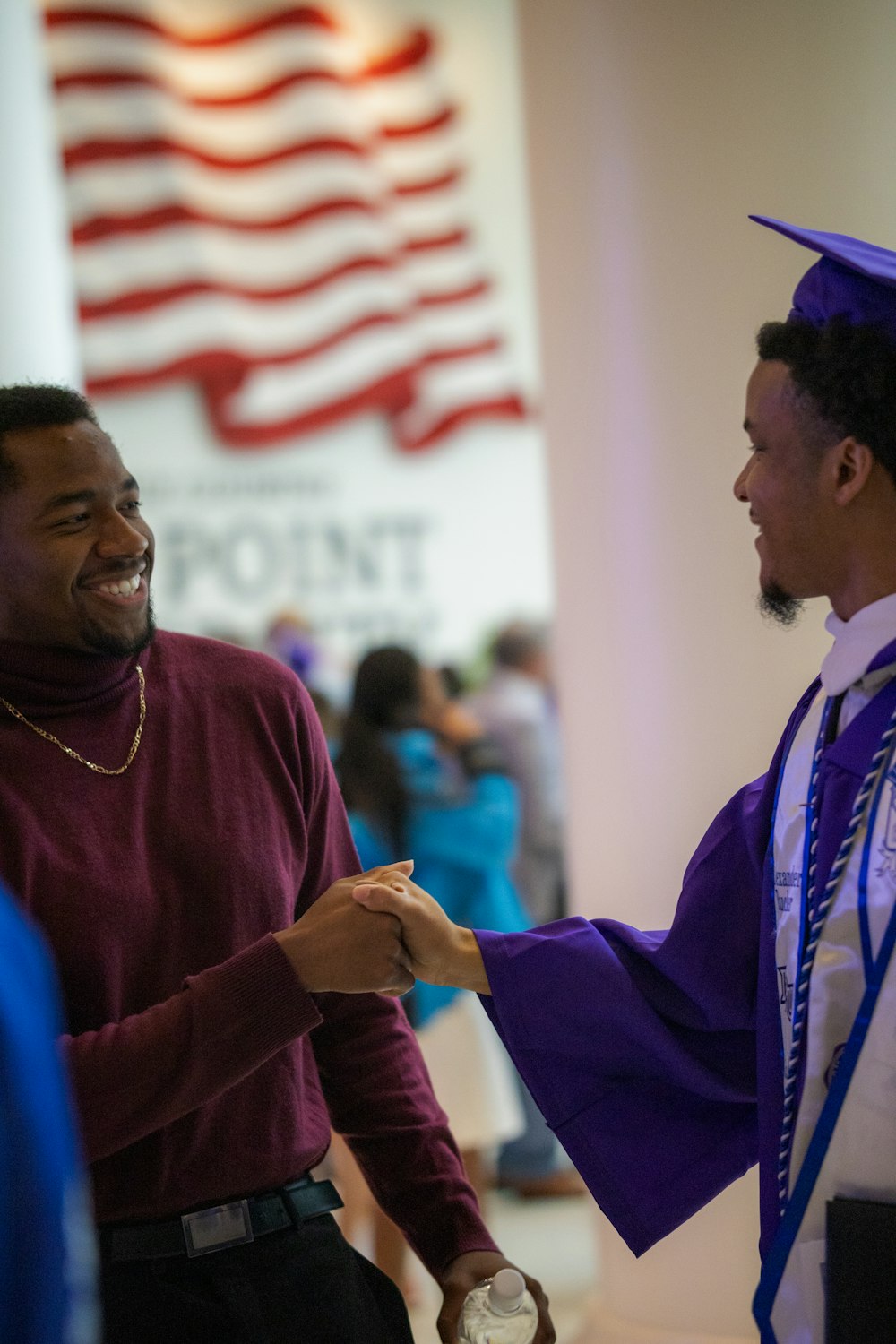 a man in a graduation cap and gown shaking hands with another man