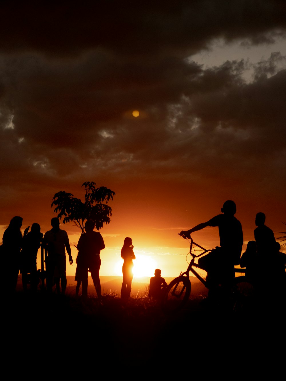 a group of people standing around a bike at sunset