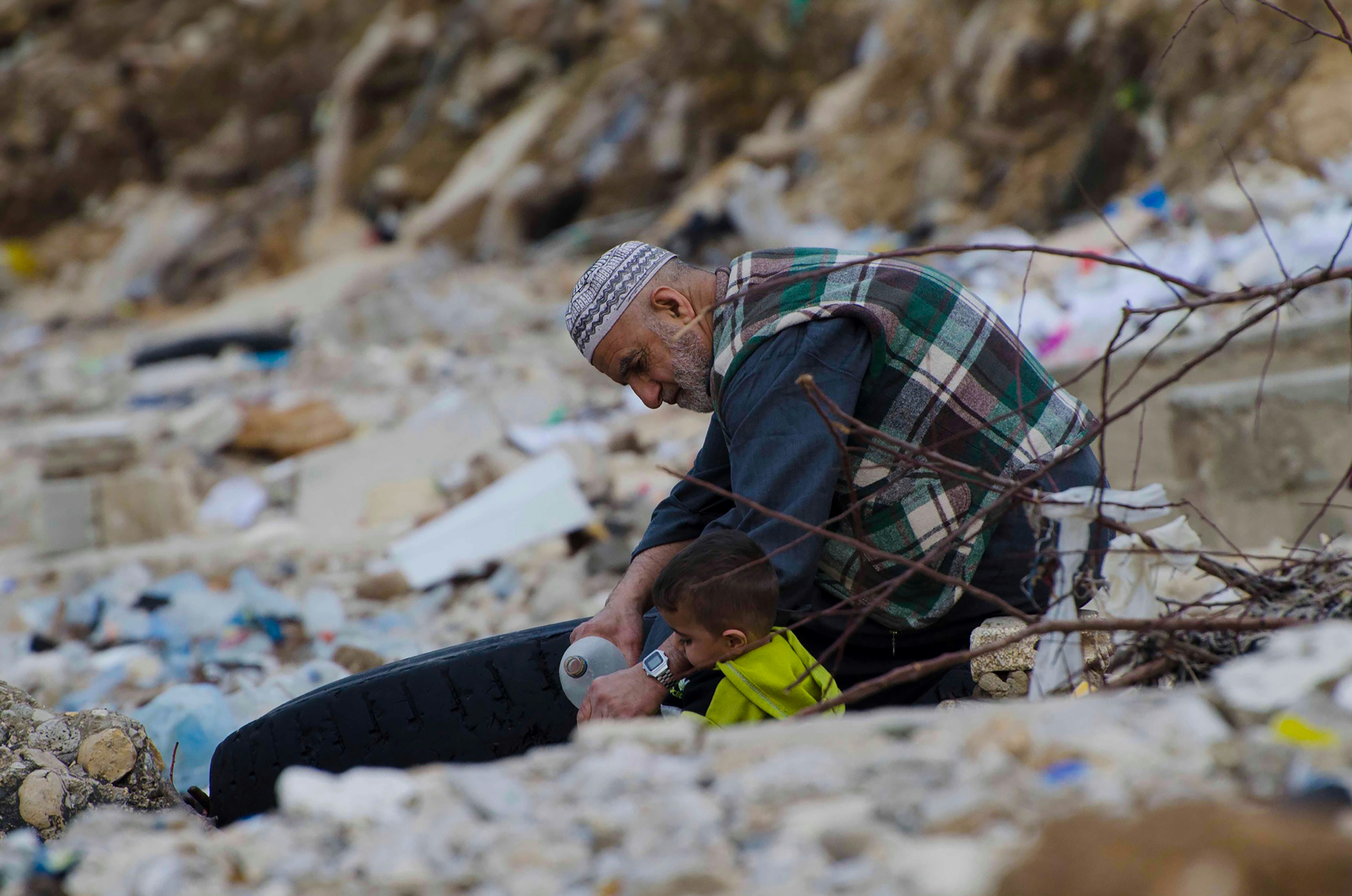 a man sitting on the ground next to a pile of trash (Photo by AHMAD BADER on Unsplash)