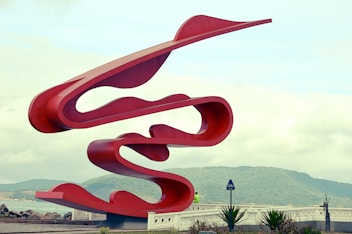 a large red sculpture sitting on top of a lush green field