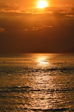 the sun is setting over the ocean with a boat in the water