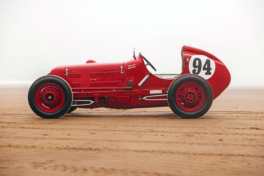 a red race car sitting on top of a dirt field