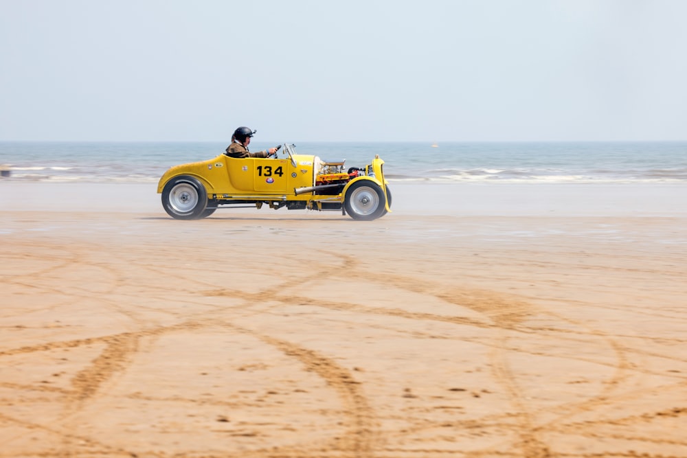 a man driving a yellow car on the beach