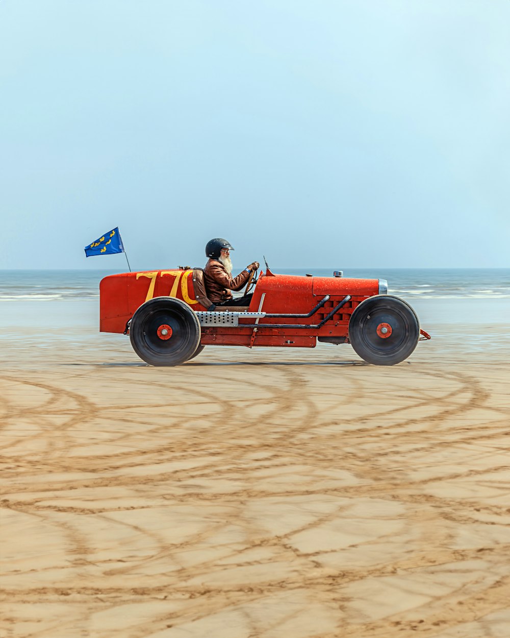 a man driving a red car on a sandy beach