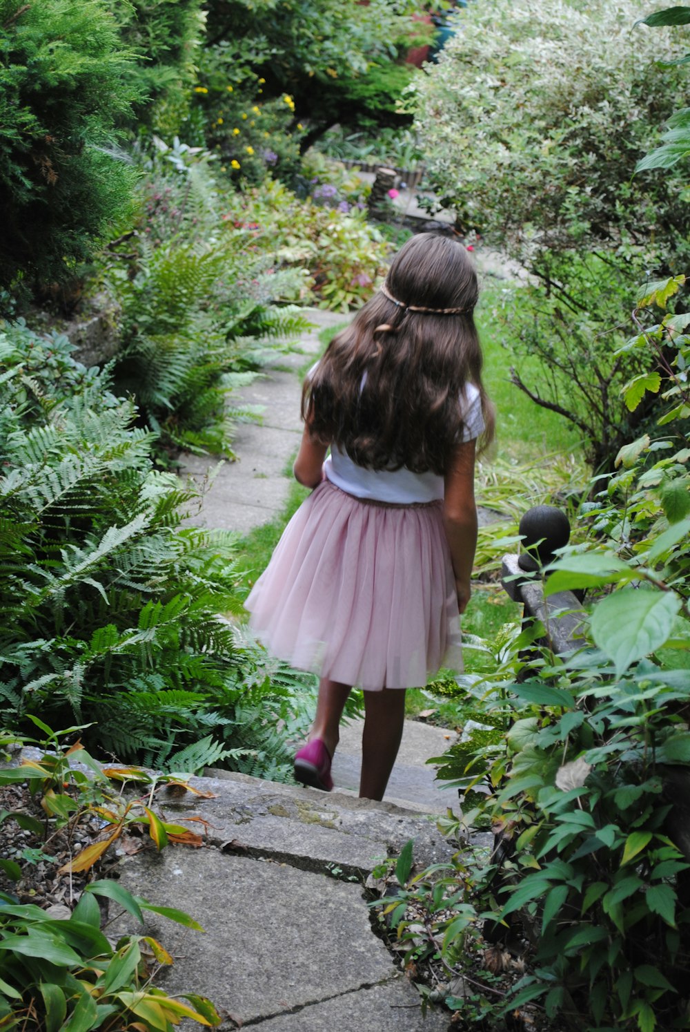 a little girl walking down a path in a garden