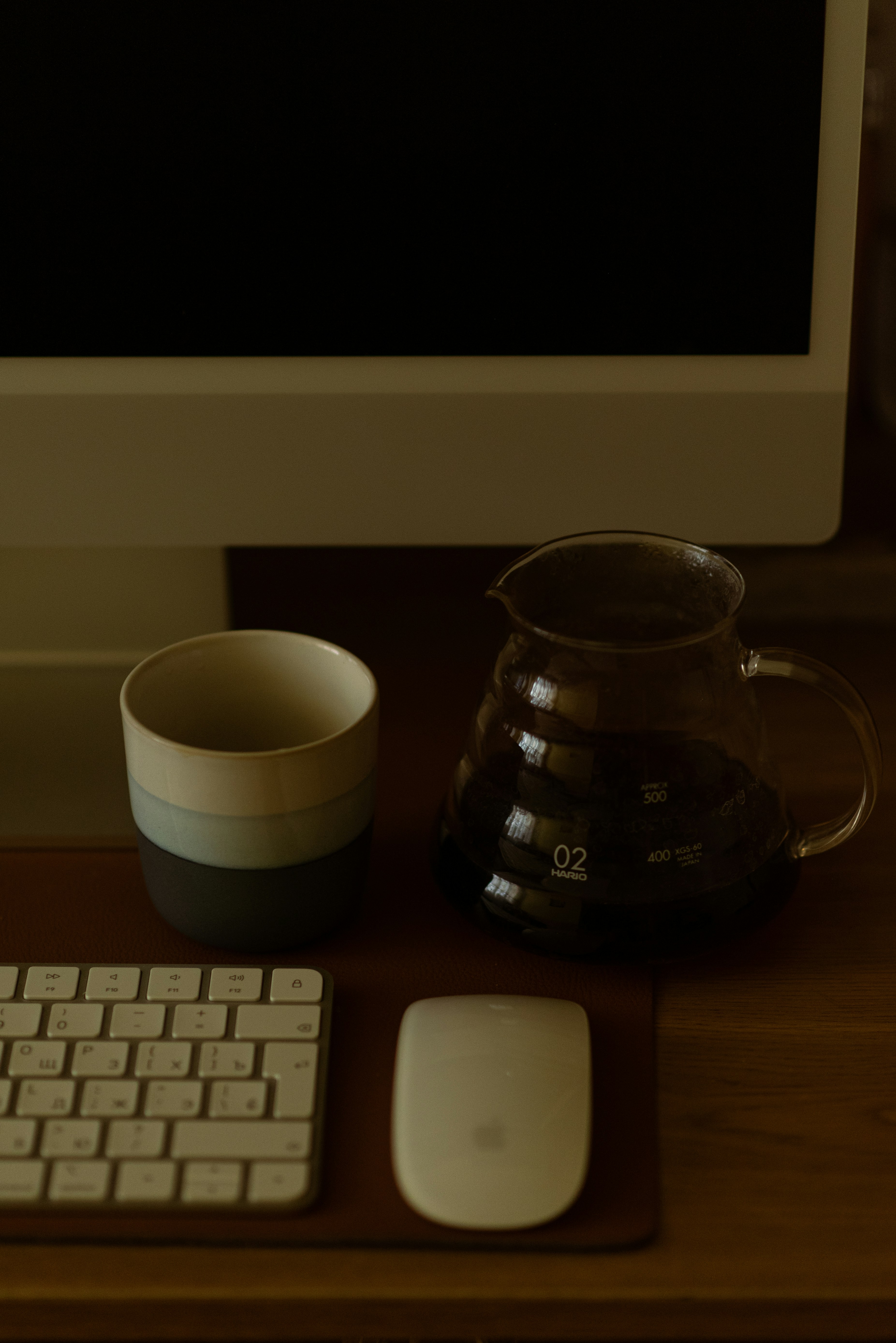 a computer monitor, keyboard, mouse and cup on a desk