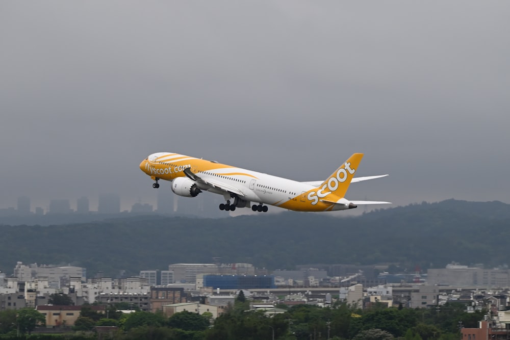 a yellow and white jet airliner flying over a city