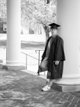 a man in a graduation cap and gown leaning against a column