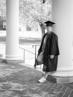 a man in a graduation cap and gown leaning against a column