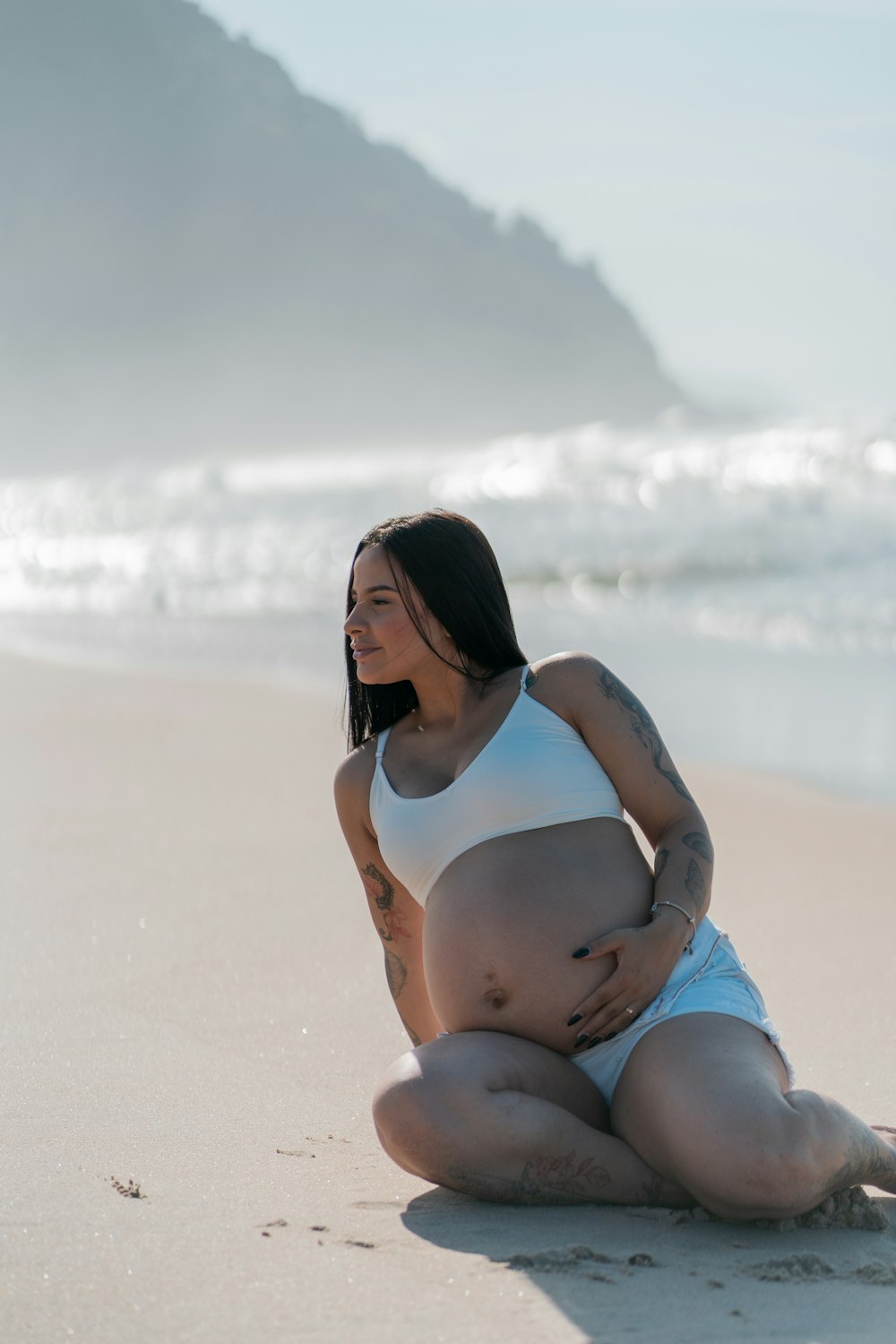 a pregnant woman sitting on a beach next to the ocean