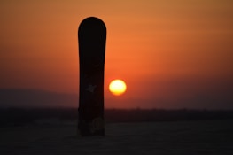 a snowboard sticking out of the snow at sunset