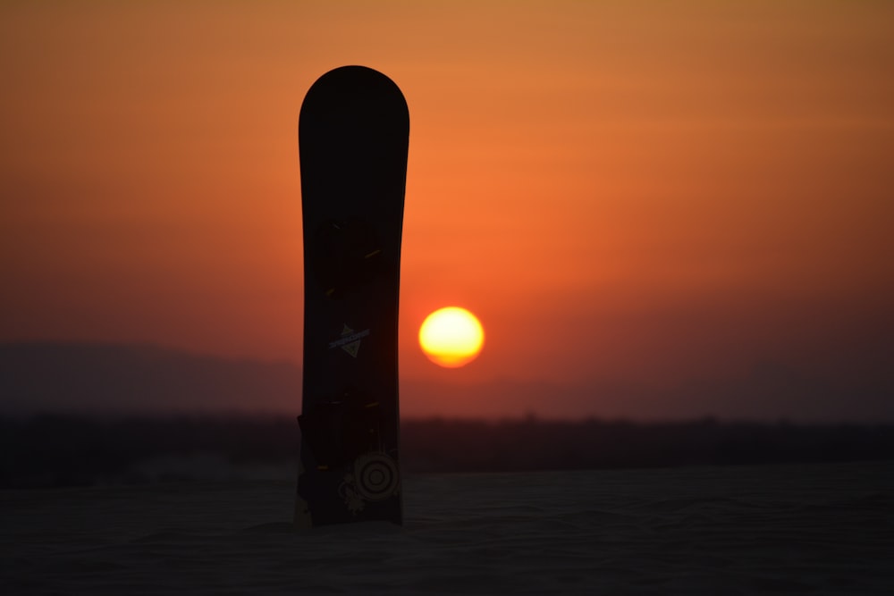 uno snowboard che spunta dalla neve al tramonto