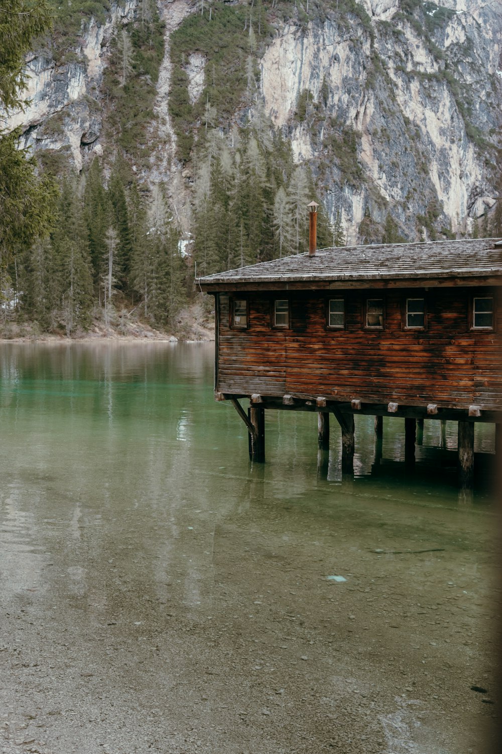a wooden cabin sitting on top of a lake next to a mountain