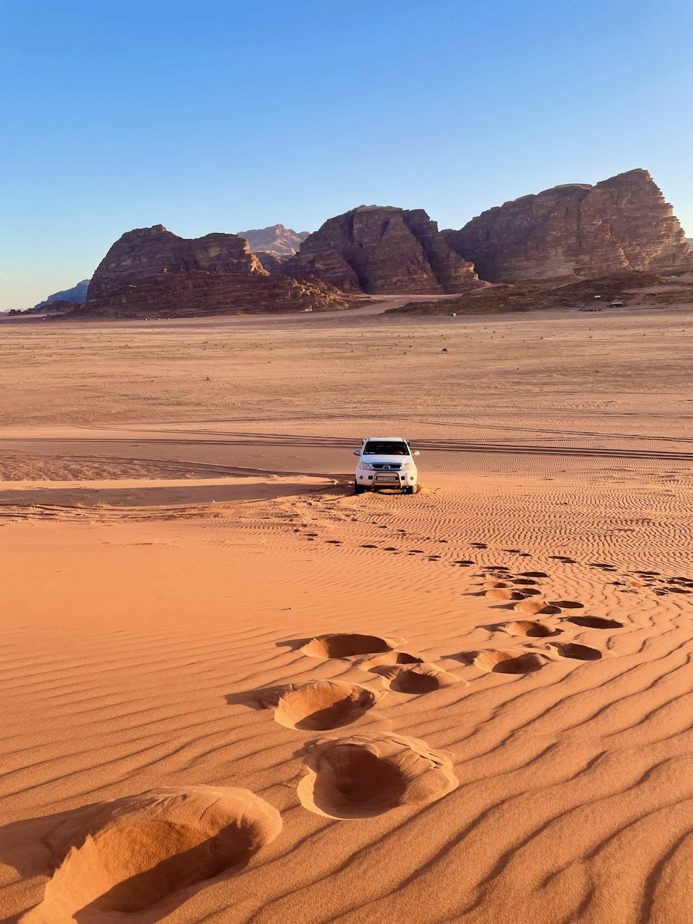 a van driving through the desert with footprints in the sand