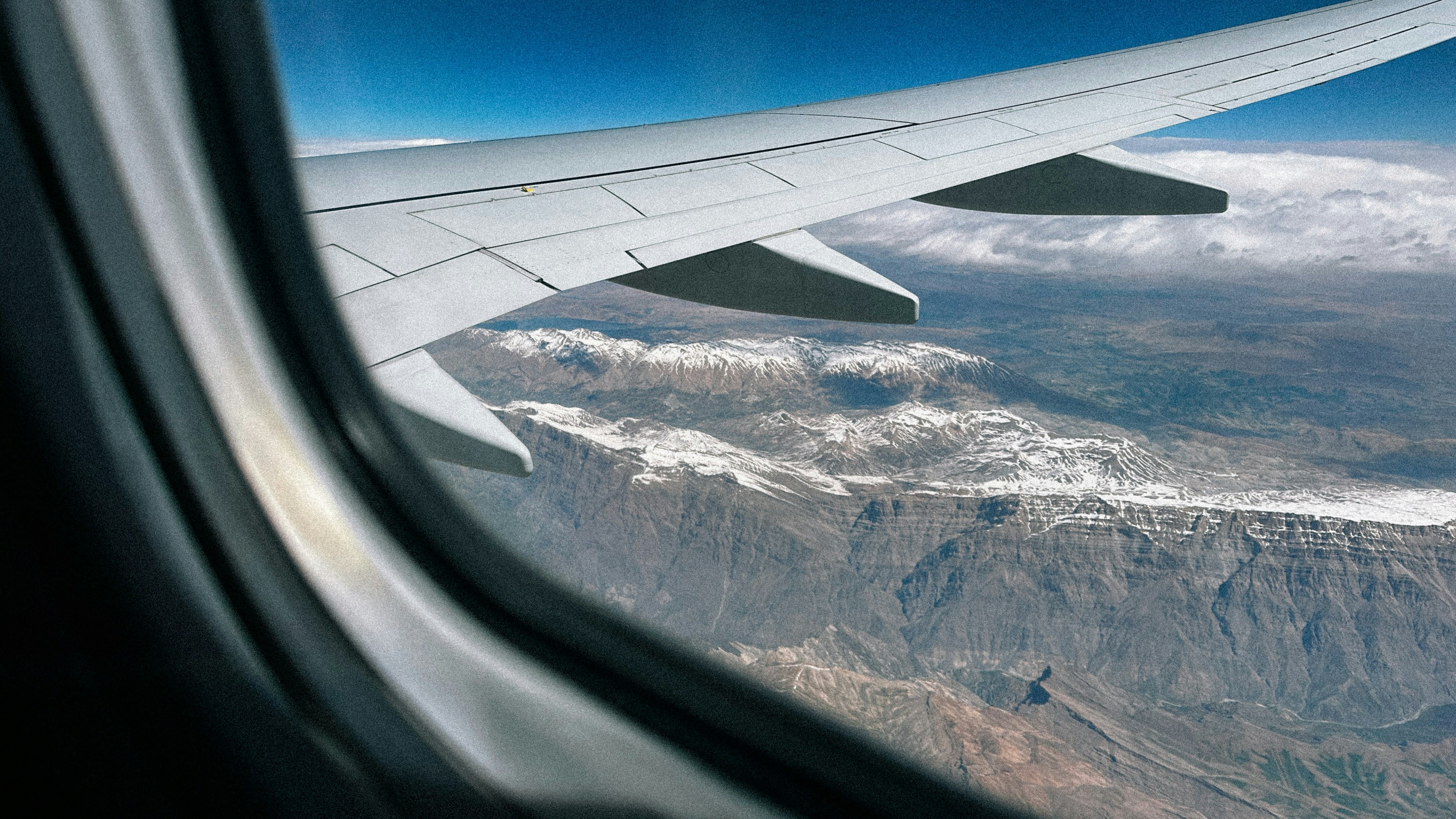a view of a mountain range from an airplane window, View of Airplane Wing Through Window