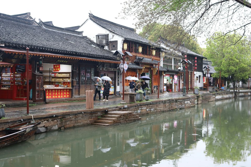 People walking down a street next to a canal in the water town of Zhujiajiao
