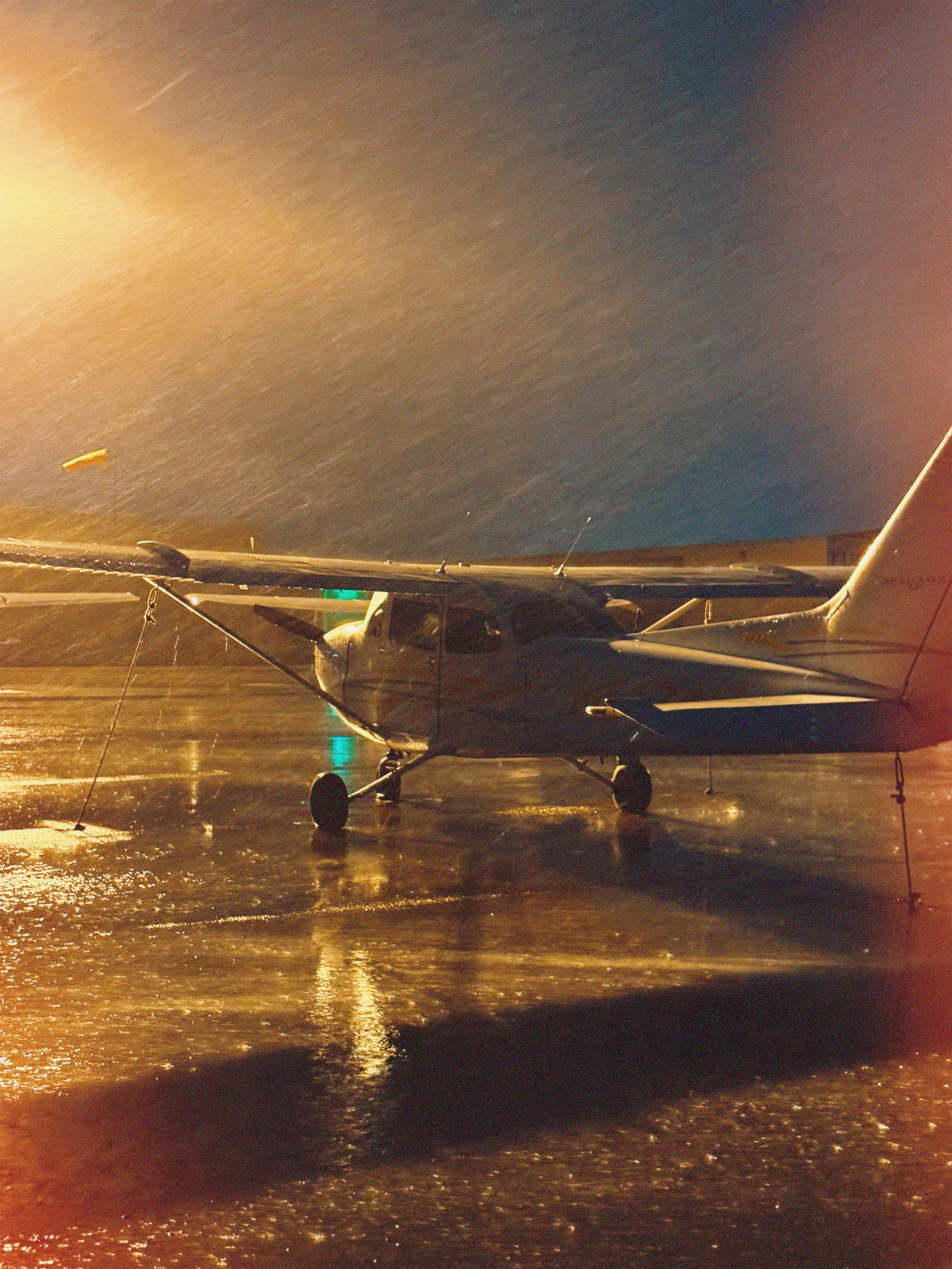 A single-engine training aircraft on a wet apron in warm evening light.