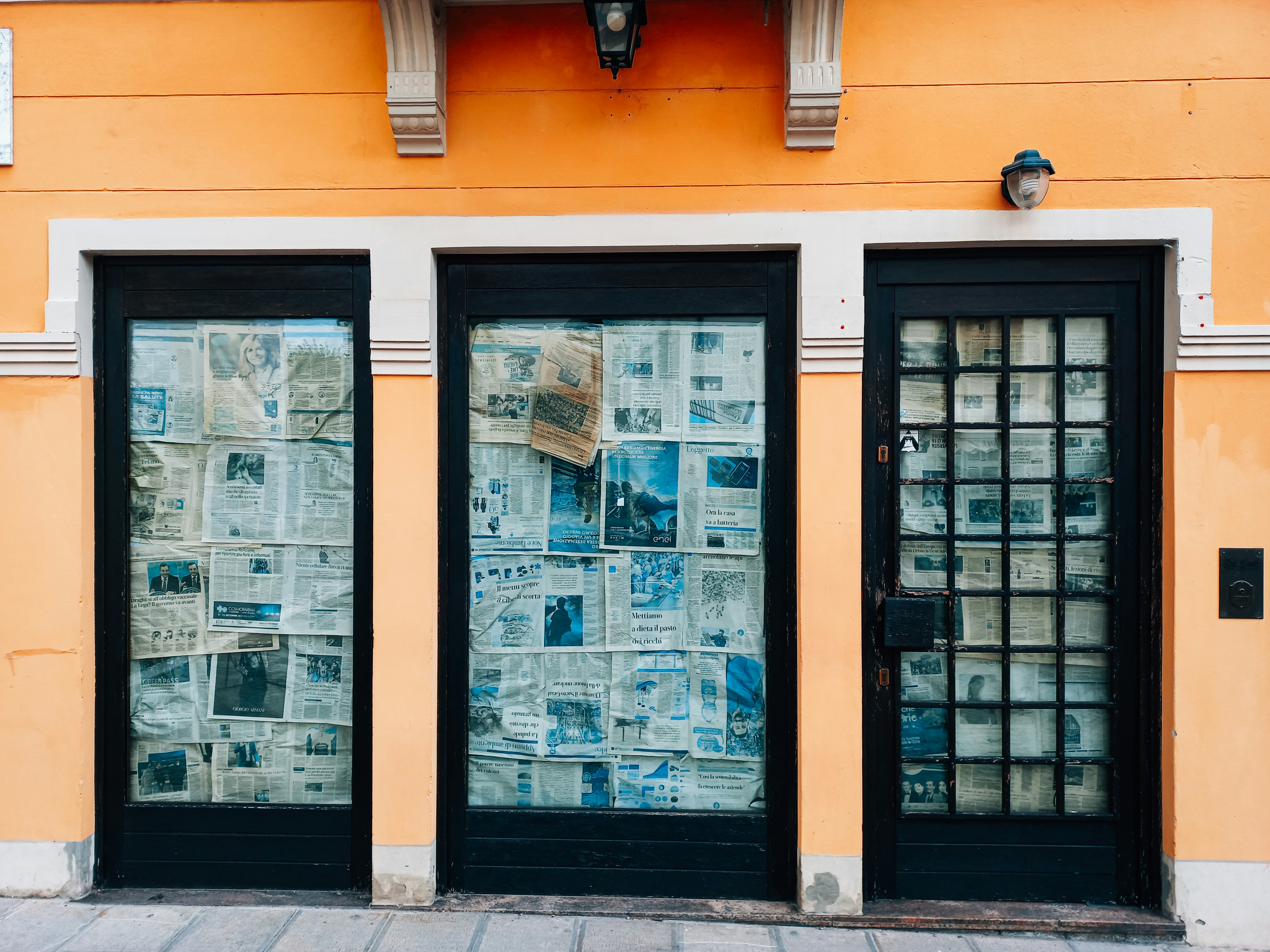 a yellow building with two black doors and a newspaper on the wall