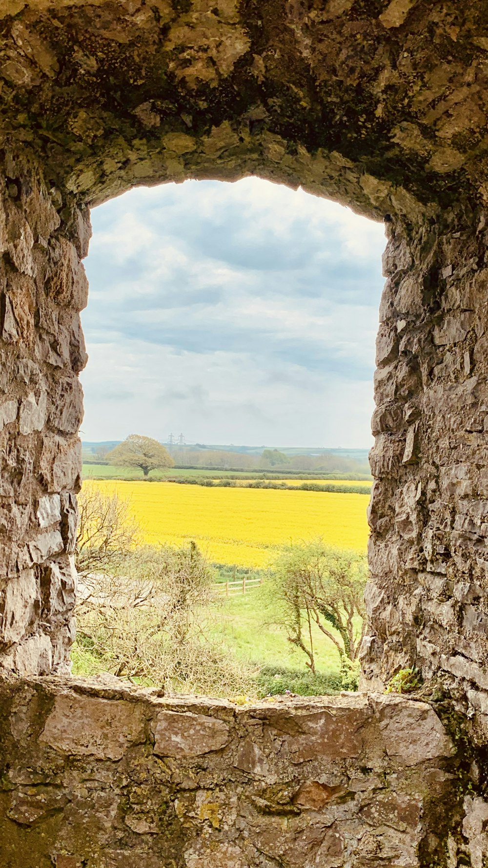 una ventana en un muro de piedra con un campo al fondo