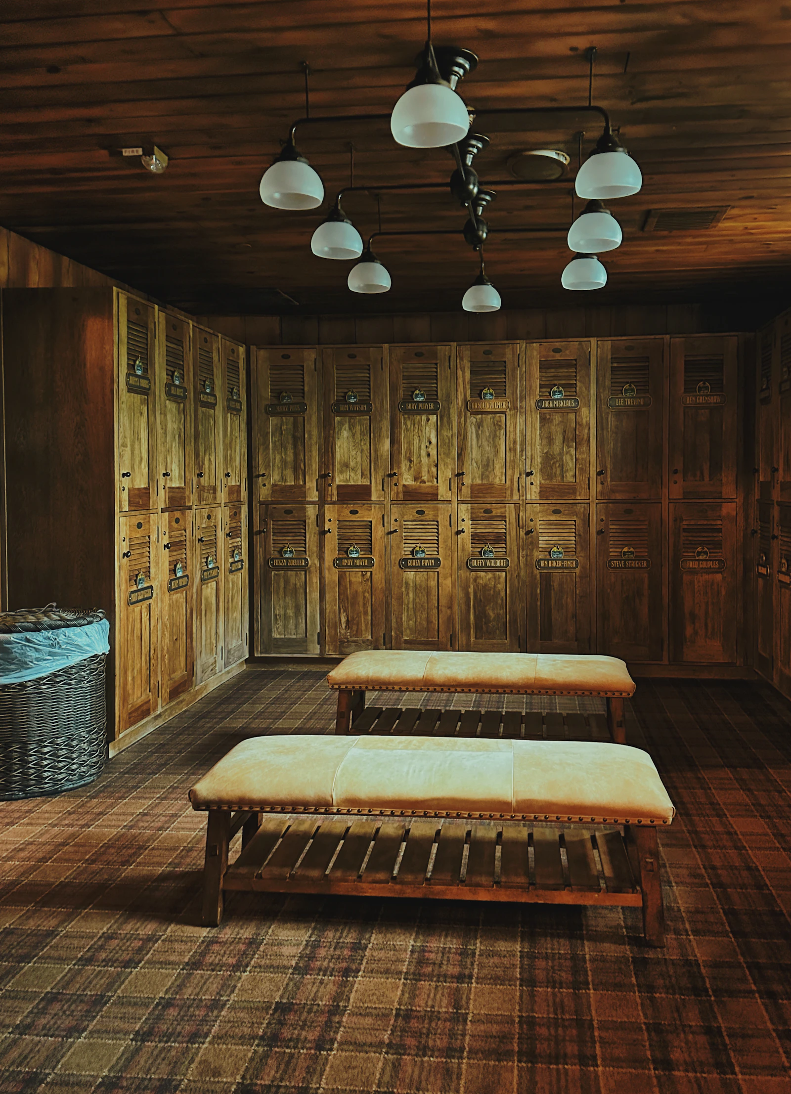 Wood-paneled locker room with named lockers and upholstered benches.