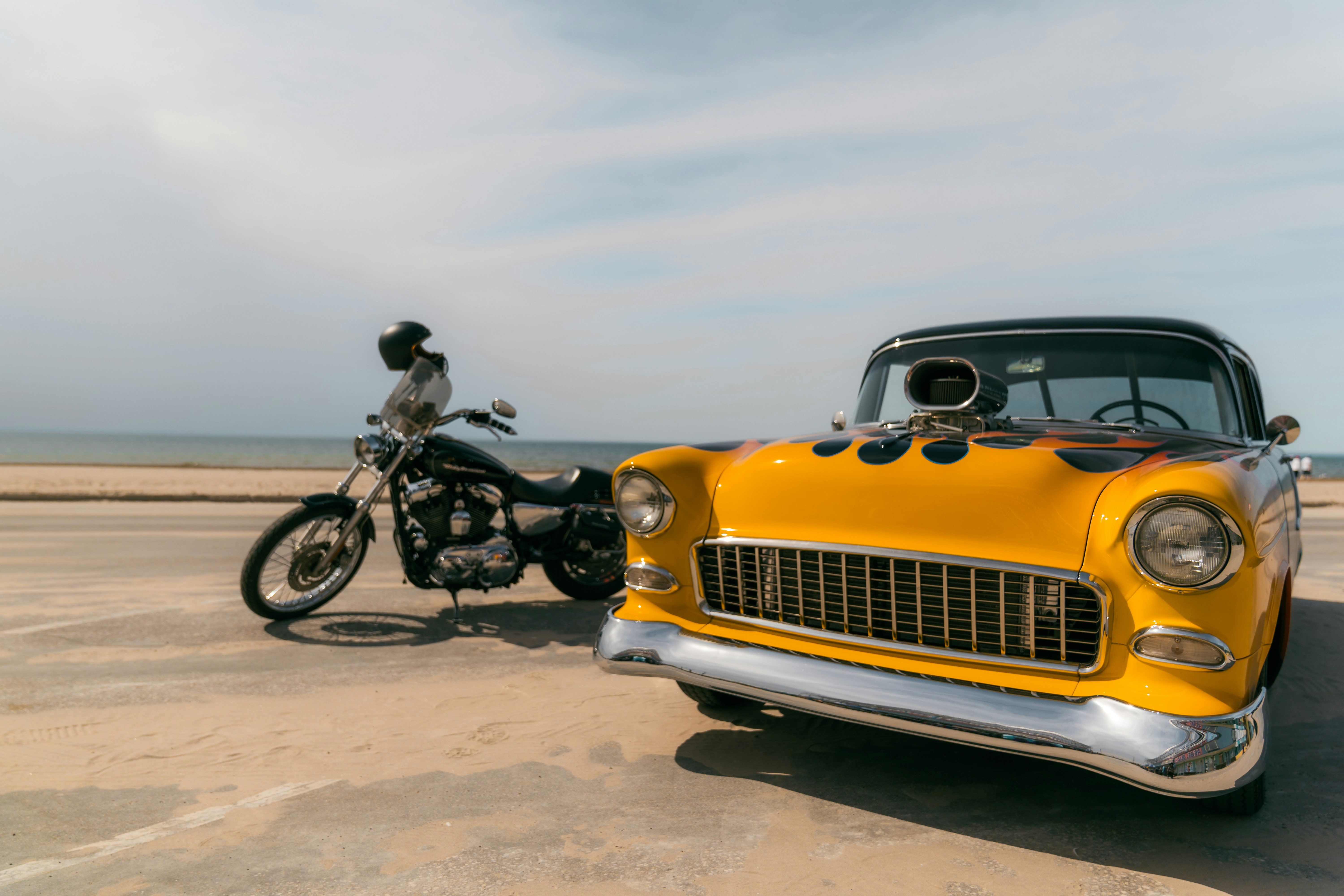 a yellow car parked next to a motorcycle on a beach