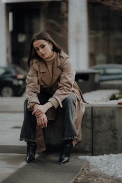 a woman in a trench coat sitting on a curb