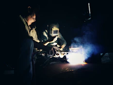 two men working on a piece of metal in the dark
