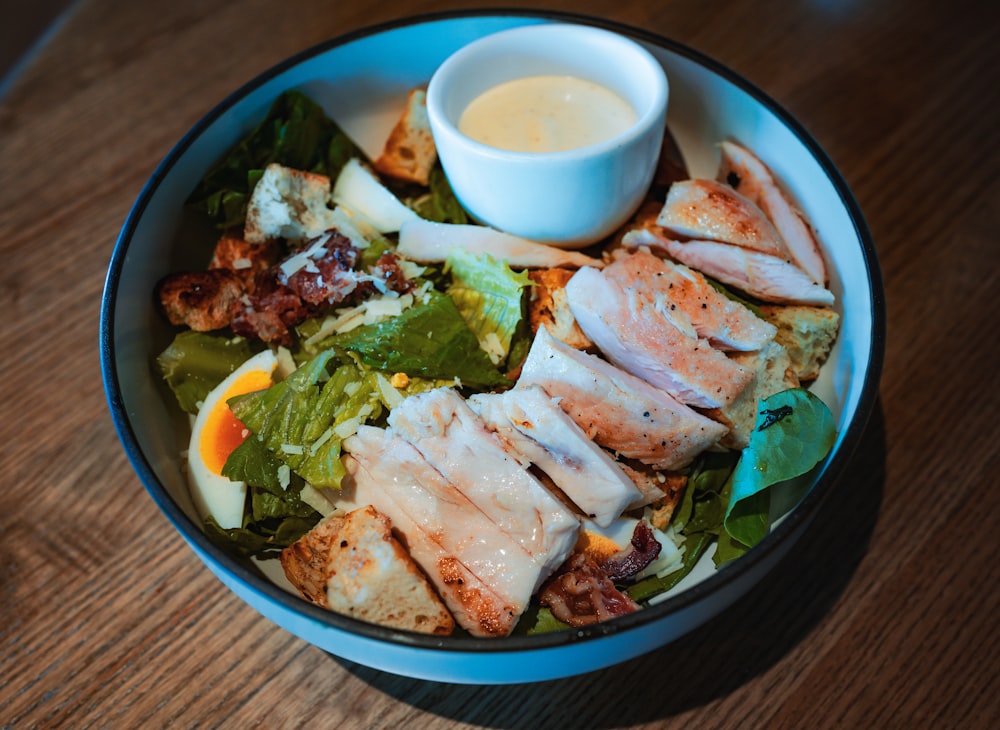 a bowl of food with chicken, lettuce, carrots, and dressing