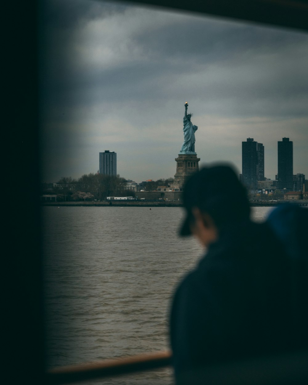 a person looking out a window at the statue of liberty