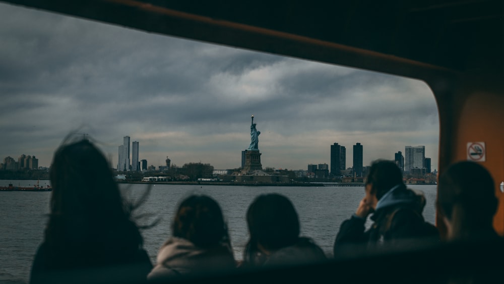 a group of people sitting on a boat looking at the statue of liberty