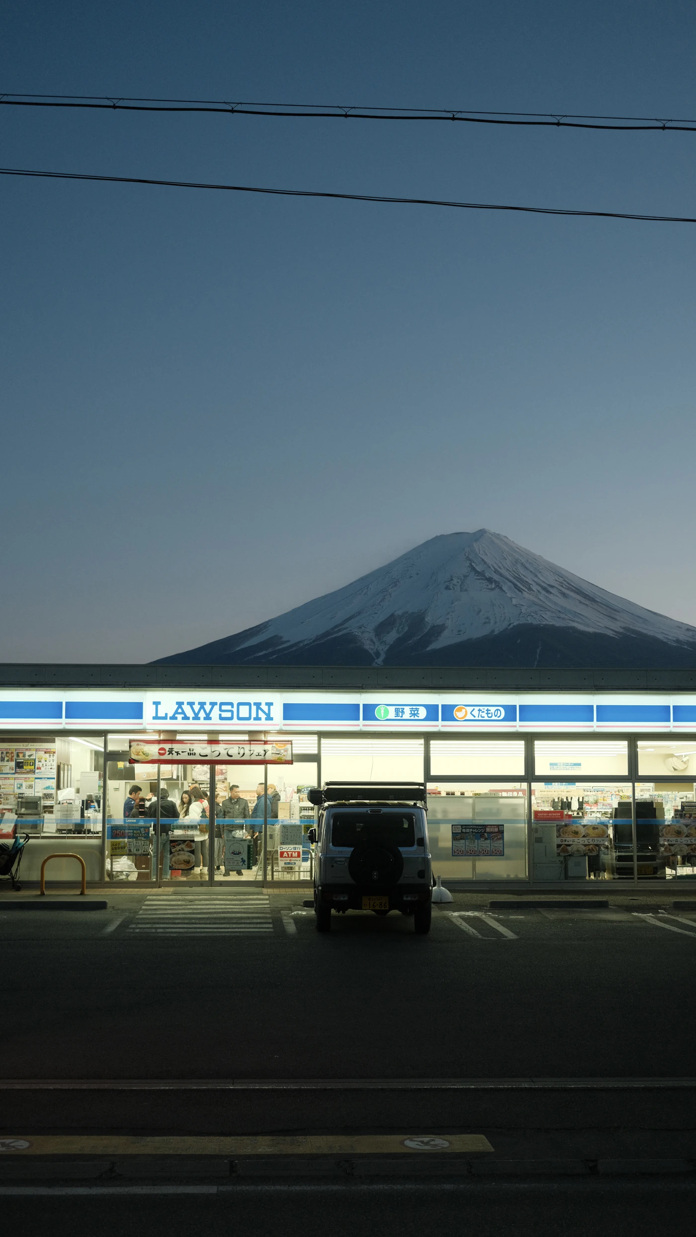 A Lawson convenience store at dusk with Mount Fuji rising behind it